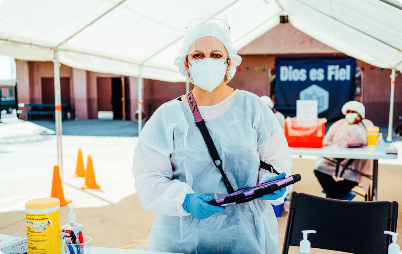 Female medical professional wearing a mask holding a tablet at a testing site