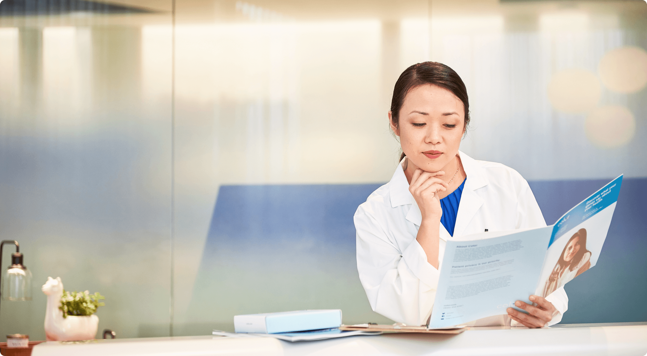 Woman wearing a lab coat sitting in an office looking at a Color brochure