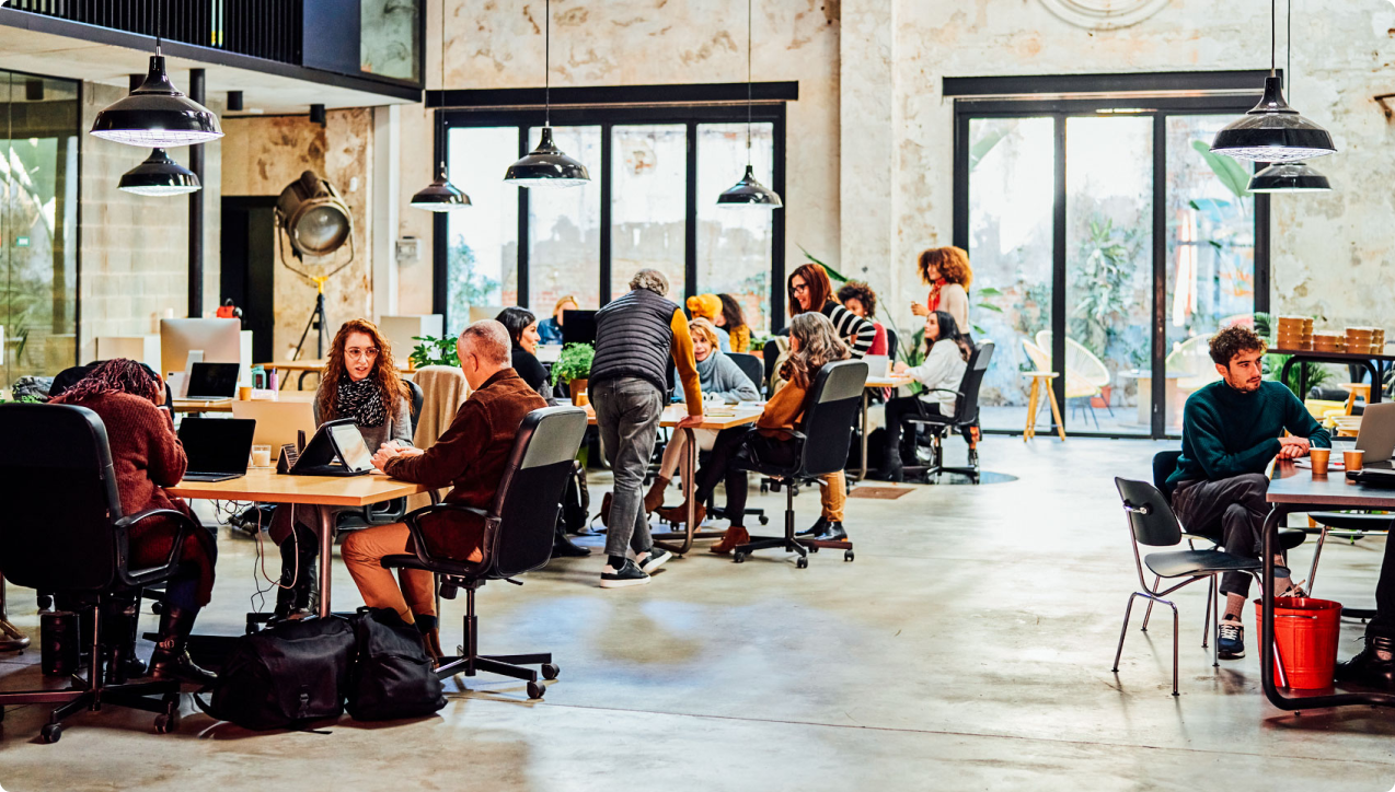 Lots of people working in an office at tables using laptops