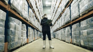 A masked person stands in a warehouse