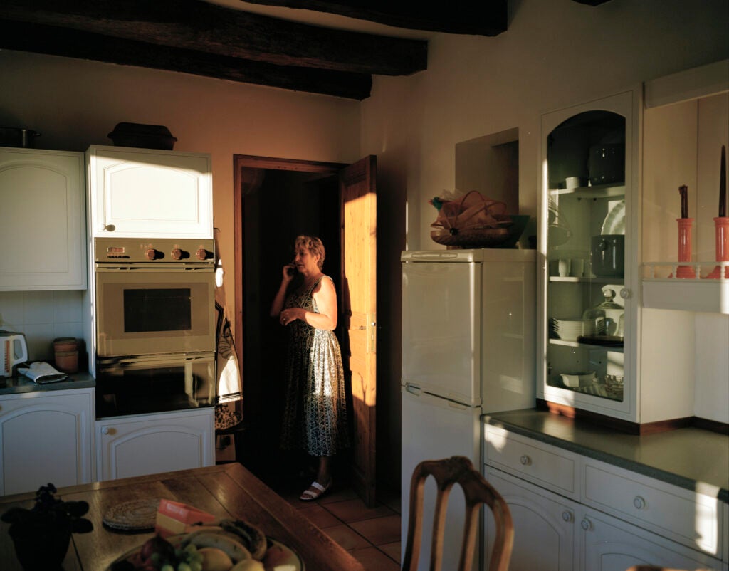 An elderly woman standing in her kitchen on a landline phone